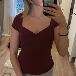 Vinröd topp - Säljer en snygg vinröd ribbad topp med korta ärmar och v-ringad hals. Säljer i bra kvalité då den blivit använd ytterst få gånger💕(spegeln är smutsig)
