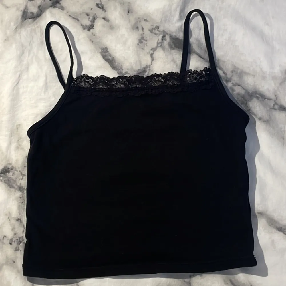 Säljer ett svart linne från H&M med spetsdetaljer längs halsringningen. Linnet har smala axelband och är perfekt för en stilren look. Tillverkat i ett mjukt och bekvämt material.. Yläosat.