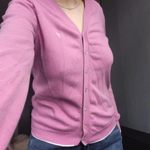 Rosa kofta från Mark Lane - söt rosa kofta från Park Lane i storlek S. Koftan har en v-ringad design med knappar framtill och långa ärmar. Fina små vita detaljer vid ärmar och tröjan slut. 💖