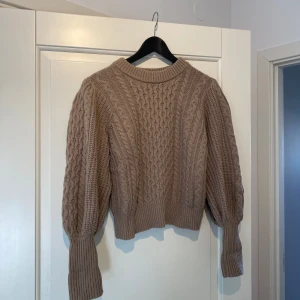 Beige stickad tröja - Säljer en mysig beige stickad tröja med flätmönster. Tröjan har långa ärmar och en rund halsringning. Perfekt för kyliga dagar!