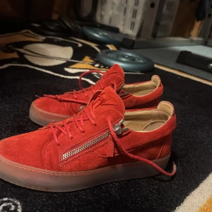 Röda sneakers från Giuseppe Zanotti - Snygga röda sneakers från Giuseppe Zanotti i mocka med dragkedja och snörning. Perfekta för att ge din stil en färgklick. Skorna har en stilren design med en bekväm sula. Kommer även med order bekräftelse och digitalt kvitto. Helt oanvända IT40