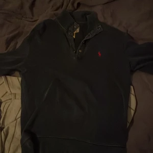 Svart pikétröja från Polo Ralph Lauren - Säljer en stilren blå pikétröja från Polo Ralph Lauren med den klassiska röda loggan broderad på bröstet. Tröjan har en knappslå med tre knappar och en krage som ger en snygg look. Perfekt för en avslappnad men ändå uppklädd stil. 100% äkta bevis finns om någon önskar, kan gå ner i pris 