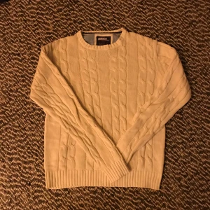 Vit kabelstickad tröja från Bondelid - Säljer en stilren beige stickad tröja från Bondelid. Tröjan har ett klassiskt flätmönster och långa ärmar. Perfekt för kyligare dagar och ger en tidlös look. Passar bra till både jeans och chinos.