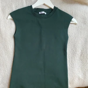 Grön ärmlös topp från Zara - Säljer en stilren grön ärmlös topp från Zara. Toppen har en rund halsringning och är tillverkad i ett mjukt material. Den är använd 3-4 gånger, skriv om frågor 💕