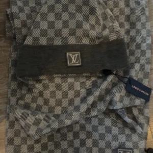 Grå mössa och halsduk från Louis Vuitton (Lv winter bundle dark edition) - Snygg grå rutig mössa och halsduk från Louis Vuitton med det ikoniska LV-emblemet framtill. Perfekt för att hålla stilen i kallare väder. Den har en klassisk passform och är tillverkad i ett mjukt material för extra komfort. Köpte denna på Vinted men passade tyvärr inte