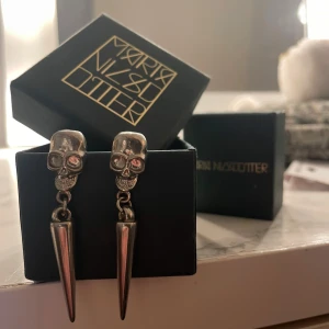 Silverfärgade dödskalleörhängen från Maria Nilsdotter - Unika örhängen i silverfärg  med dödskallemotiv och hängande spetsdetaljer. Perfekta för att ge en edgy touch till din stil. Maria Nilsdotter vibe, men märket är okänt.❤️❤️