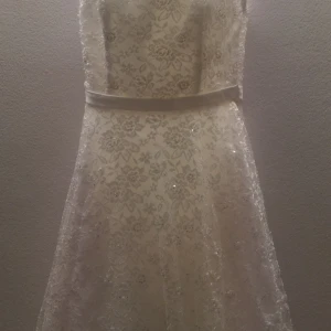 Vit spetsklänning med blommönster - Elegant vit klänning med vackert blommönster i spets och en smickrande midjeband. Perfekt för speciella tillfällen med sin romantiska design och detaljerade spetsarbete.