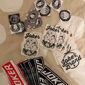 Klistermärken från Joker Brand - Ett set med olika klistermärken från Joker Brand. Innehåller både runda och rektangulära märken med olika motiv, inklusive en clown och Joker Brand-logotypen. Perfekt för att dekorera dina tillhörigheter med en unik stil.