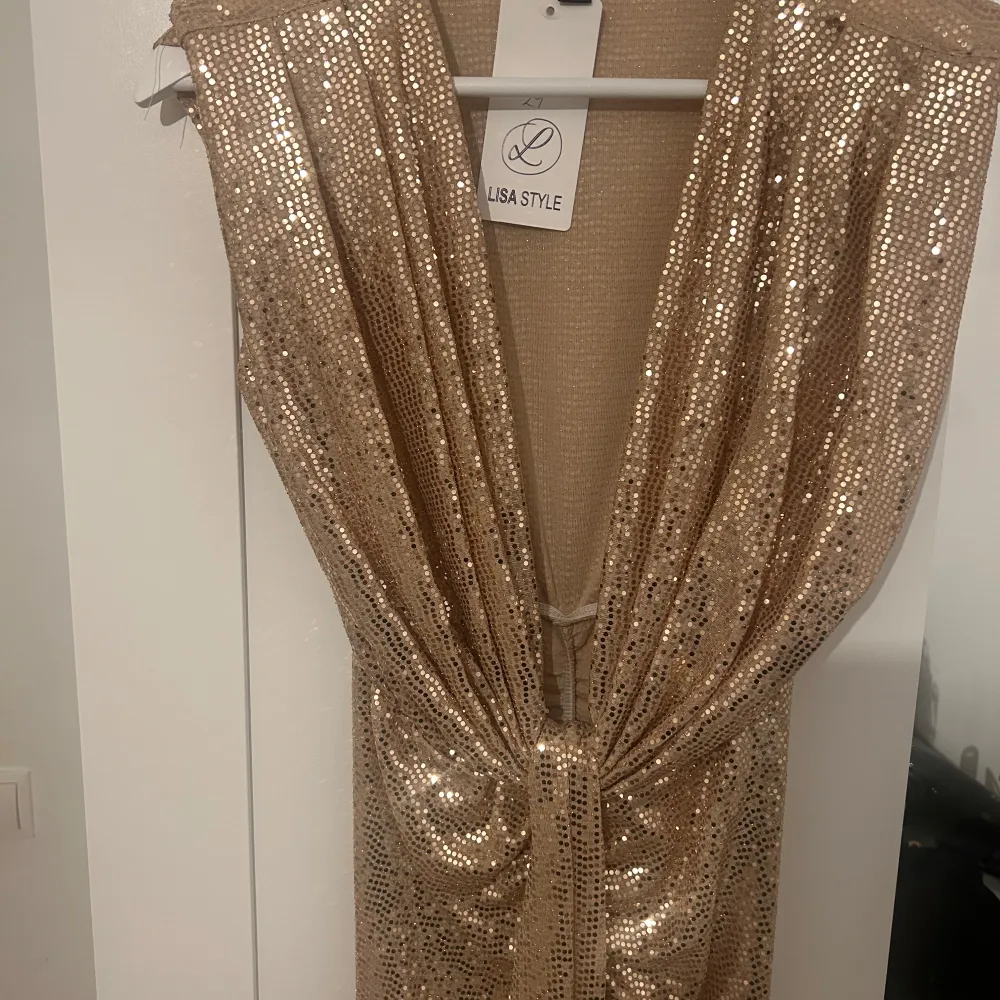 Snygg glittrig guldklänning från Lisa Style. Klänningen har en djup v-ringning och är täckt med paljetter som ger en glamorös look. Perfekt för att sticka ut på festen! ✨. Mekot.