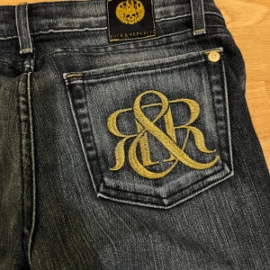 Mörkblå jeans från Rock & Republic - Snygga mörkblå jeans från Rock & Republic med broderad logga i guld på bakfickorna. Byxorna är bootcut och väldigt sköna. 