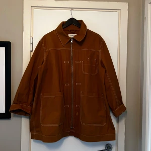 Jacka från Weekday - Säljer en snygg brun workwear jacka från Weekday i storlek S. Jackan har en dragkedja framtill och stora fickor. Perfekt för höst och vår med sin stilrena design och långa ärmar.