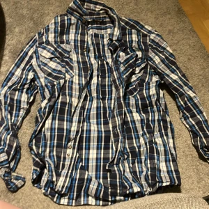 Blårutig skjorta från Tuxer - Säljer en snygg blårutig skjorta från Tuxer i storlek XXL. Skjortan har långa ärmar och knappar framtill samt på bröstfickorna. Perfekt att ha endast över till eller ha som en kofta över något. Pris kan alltid diskuteras, skriv till mig för övriga frågor eller bilder!