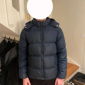 Mörkblå pufferjacka från Tommy Hilfiger - Säljer en snygg mörkblå pufferjacka från Tommy Hilfiger. Riktigt varm och skönt, fin broderad logga där fram och på sidan. Riktigt stilig! Hör av dig vid fler frågor eller funderingar!