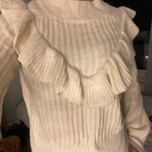 Stickad tröja med volangdetaljer - Säljer en söt  stickad tröja med volangdetaljer runt halsen. Tröjan har långa ärmar och en ribbad struktur som ger en mysig känsla. Perfekt för kyligare dagar!☺️☺️