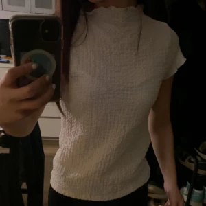 Vit ribbad topp - Säljer en vit ribbad topp med korta ärmar och hög hals. Toppen har en texturerad yta som ger en unik look. Perfekt för att styla med jeans eller kjol. Har ett litet hål vid halsen men annars inga tecken på använd💞Nypris ca 300kr säljes för 120kr, kom gärna med prisförslag!