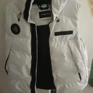 Vit dunväst från Sail Racing - Säljer en snygg vit dunväst från Sail Racing i mycket bra skick. Västen har en praktisk huva och dragkedja framtill. Perfekt för kyliga höst- och vårdagar. Den är stilren och passar till många olika outfits.