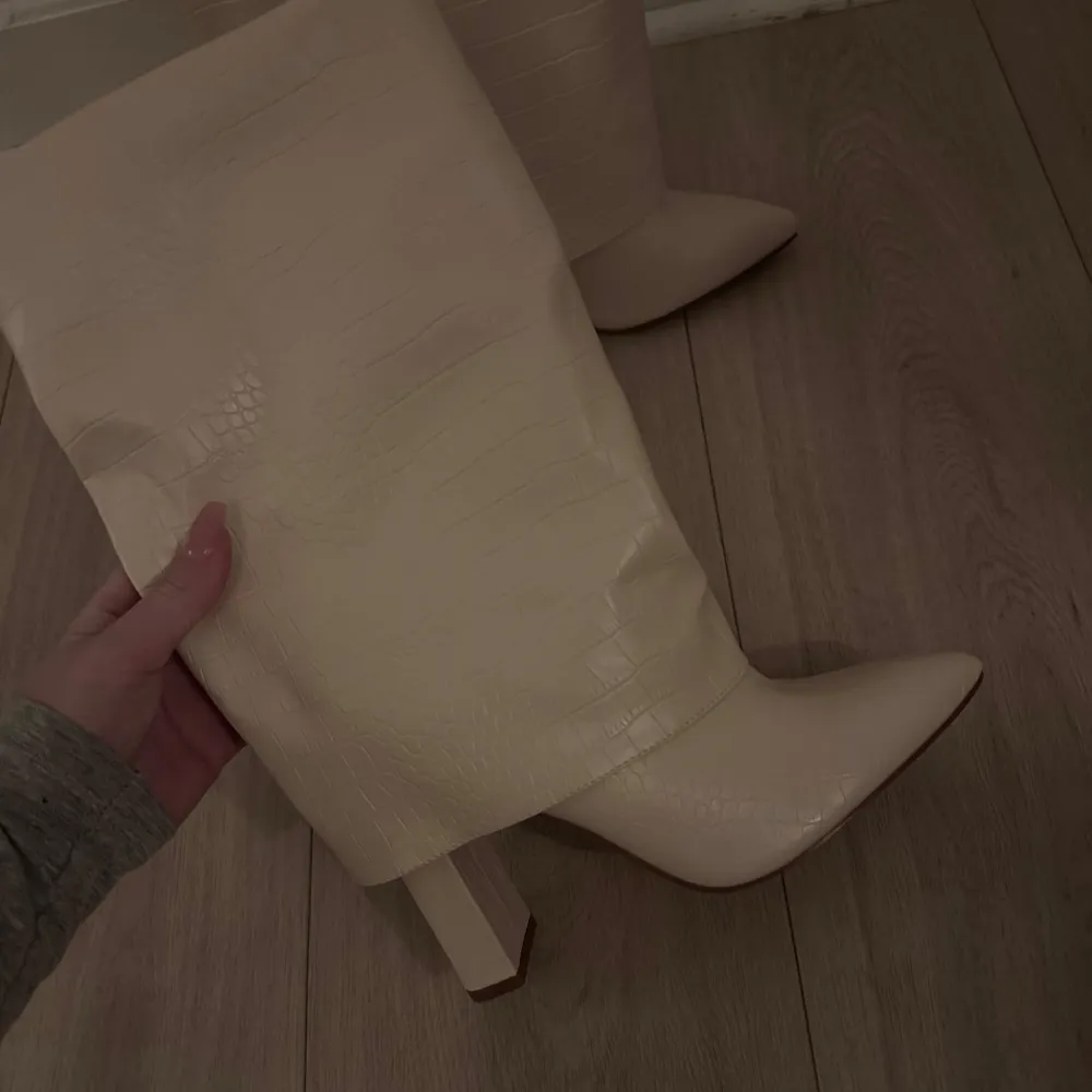 Säljer ett par eleganta beige stövlar i syntetmaterial. De har en spetsig tå och en stabil klack, perfekt för både vardag och fest. Stövlarna är i nyskick (helt oanvända) och har en stilren design som passar till många olika outfits.. Kengät.