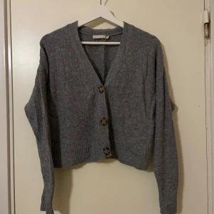 Cardigan Kofta - Säljer en mysig grå kofta i storlek S. Den har stora knappar framtill och är perfekt för kyliga dagar. Koftan är i ett mjukt material och har en klassisk design som passar till det mesta. Perfekt för höst och vinter!