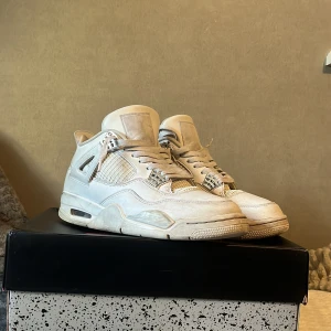 Air Jordan 4 Retro White/Metallic Silver - Säljer ett par Air Jordan 4 Retro i färgen vit med metallic silver detaljer. Skorna är i bra skick och kommer med originalkartong. Perfekta för både vardag och fest! 🏀✨