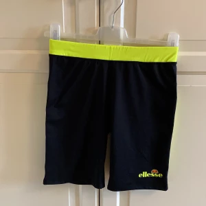 Svarta träningsshorts från Ellesse - Säljer ett par svarta träningsshorts från Ellesse med en cool neongul linning och sidodetaljer. Perfekta för gymmet eller löprundan! De är bekväma och har en elastisk midja för bästa passform. Loggan syns tydligt på benet. 🏃‍♀️Storlek 38. I fint skick. 