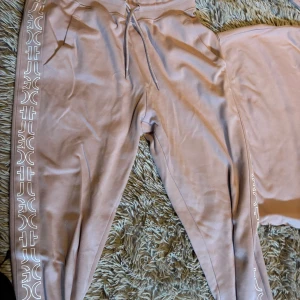 Hugo rosa mjukisbyxor med tryck  - Säljer ett par snygga rosa mjukisbyxor med coolt tryck längs sidorna. De har en bekväm passform med snörning i midjan. Perfekta för en avslappnad dag hemma eller en snabb tur till affären. Materialet känns mjukt och skönt mot huden.