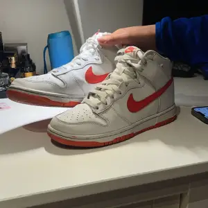 Säljer ett par Nike Dunk High i vitt med röda detaljer. Skorna har en klassisk hög design med snörning och en röd sula. Perfekta för både vardag och träning. De är i bra skick med lite slitage på sulan. Storlek 41. Men passar även folk med storlek 40-42.