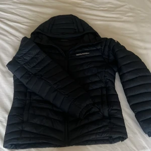 Mörkblå  dunjacka från Peak Performance - Säljer en mörkblå dunjacka från Peak Performance. Jackan har en quiltad design med dragkedja framtill och en justerbar huva. Perfekt för kyliga dagar med sin stilrena look och funktionella detaljer. Sprillans ny, nypris 3199. Pris kan diskuteras