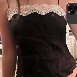 Svart linne med spetsdetaljer från Zara - Säljer ett stilrent svart linne från Zara med vacker vit spets upptill. Linnet har smala axelband och en elegant passform. Perfekt för en chic look!