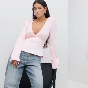Ljusrosa omlottopp - Säljer en ljusrosa omlottopp med v-ringning och långa ärmar. Toppen har en knytning i ryggen som ger en fin passform. Perfekt för en stilren look.