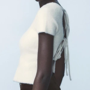 Vit stickad topp med öppen rygg - Säljer en stilren vit stickad topp med korta ärmar och en unik öppen ryggdesign med snörning. Perfekt för att ge en elegant touch till din outfit. Toppen är mjuk och bekväm att bära.