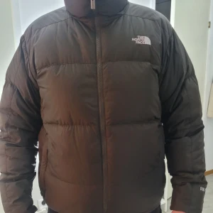 Miltärgrön/grön melerad dunjacka från The North Face - Säljer en militärgrön/grön melerad dunjacka från The North Face med dragkedja och broderad logga på bröstet. Jackan har en puffig design och är perfekt för kalla dagar. Den har långa ärmar och är märkt med '550' på ärmen, vilket indikerar dunfyllningens kvalité stl: L personen på bilden är 186cm och 90kg 