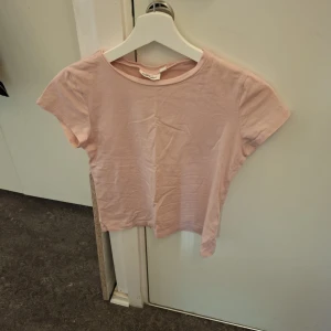 Rosa kortärmad topp - Säljer en söt rosa kortärmad topp från Kappahl. Den är enkel och stilren, perfekt för en avslappnad look. Toppen har en rund halsringning och är gjord i ett mjukt material.