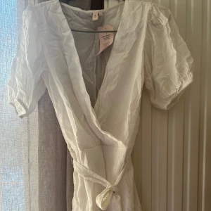 Vit omlottklänning från Nelly - Säljer en stilren vit omlottklänning från Nelly. Klänningen har korta ärmar och ett knytband i midjan för en smickrande passform. Perfekt för varma dagar och somriga tillfällen speciellt till studenten. 💫 Köparen står för frakten! Pris kan diskuteras💖