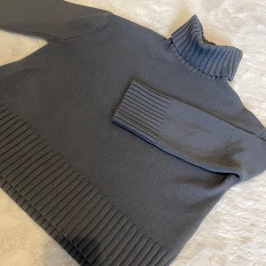 Grå stickad polotröja - Säljer en stilren grå stickad polotröja med ribbade detaljer vid krage, ärmslut och nederkant. Perfekt för kyliga dagar och ger en mysig känsla. Passar bra till både jeans och kjol. Ett måste i garderoben för höst och vinter!