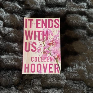 It Ends With Us - Säljer boken 'It Ends With Us' av Colleen Hoover. Omslaget har en ljus bakgrund med rosa blommor och stor rosa text. Perfekt för dig som gillar romantiska och känslosamma berättelser.