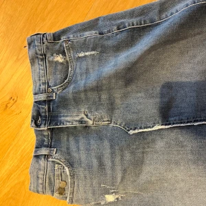 Blå jeans kjol från Odd Molly - Snygg blå kjol från Odd Molly med slitna detaljer och klassisk femficksdesign. De har en knappgylf och är perfekta för en avslappnad stil. Passar bra till både sneakers och boots.