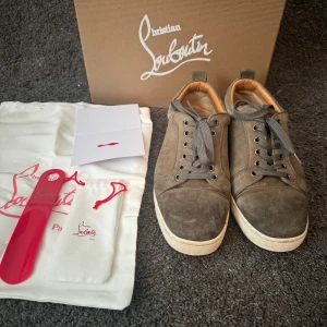 Gröna sneakers från Christian Louboutin - Snygga gröna sneakers från Christian Louboutin med den ikoniska röda sulan. Skorna har snörning och är tillverkade i skinn. Perfekta för dig som vill ha en stilren look med en touch av lyx.