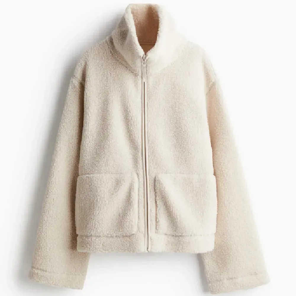 Mysig beige teddyjacka med dragkedja framtill och stora fickor. Perfekt för kyliga dagar med sin fluffiga och varma design. Jackan har en hög krage och långa ärmar för extra komfort.den har ett litet sy märke som inte syns . Takit.