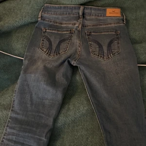 Blå jeans från Hollister - Snygga blå low-rise bootcut jeans från Hollister. De har en klassisk femficksdesign och en bekväm stretch. Passar någon som är 155-165.