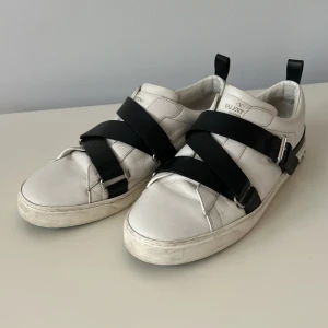 Valentino sneakers med svarta remmar - Snygga vita Valentino garavani sneakers med svarta remmar som är i ett mycket bra skick och har alla nitar kvar!   Strl 44, Hör gärna av dig om du har några frågor eller funderingar!!