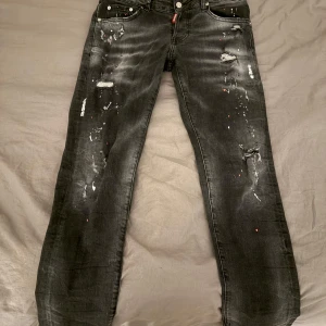 Svarta jeans från Dsquared2 - Snygga svarta jeans från Dsquared2 med slitna detaljer och en cool, distressed look. Jeansen har en klassisk femficksdesign och en knappgylf. Perfekta för en trendig och avslappnad stil.