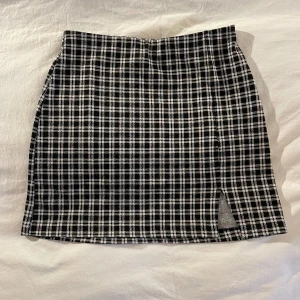 Svartvit rutig kjol från H&M - Snygg svartvit rutig kjol från H&M med en liten slits på framsidan. Perfekt för en stilren look. Kjolen har en kort längd och är i en klassisk passform.