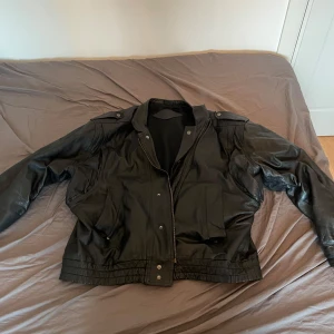 Svart skinnjacka  - Snygg svart skinnjacka med en klassisk look. Jackan har långa ärmar och knappar framtill. Perfekt för en cool och stilren outfit. Den har en ribbad nederkant som ger en bra passform. Den är av bra italiensk läder. köpte i italien för några år sen och vill sälja nu den var dyr då då den är äkta läder men är använd så säljer billigare. Den är i otroligt bra skick vilket visar på de bra materialet