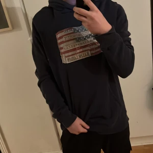 Mörkblå hoodie från Ralph Lauren - Säljer en snygg mörkblå hoodie från Ralph Lauren med ett stort amerikanskt flaggmotiv på bröstet. Unik och väldigt stilren