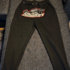 Svarta mjukisbyxor från Trapstar - Säljer ett par svarta mjukisbyxor från Trapstar med tryck på framsidan. Byxorna har snörning i midjan för justerbar passform. Perfekta för en avslappnad stil.