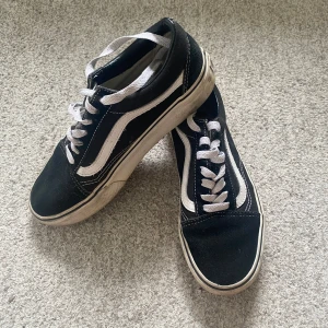 Svarta sneakers från Vans st 38 - Säljer ett par klassiska svarta Vans sneakers med vit sula och vita snören. Skorna har den ikoniska vita sidostripen och 'Off the Wall'-loggan på hälen. Storlek 38