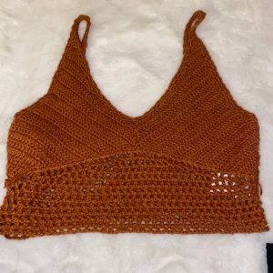 Brun stickad linnetopp - Säljer en brun/orange stickad linnetopp med smala axelband och v-ringad design. Toppen har ett luftigt mönster nedtill som ger en snygg look. Perfekt för varma dagar!
