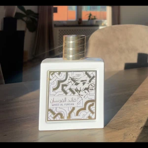 Qaed Al Fursan parfym - 100 ML varav ca 95 ML kvar. Elegant parfymflaska i vitt med guldlock och dekorativ etikett. Doften är från Lattafa och heter Qaed Al Fursan. Toppnoter: Kokos, Citrus & Ananas Hjärtnoter: Ylang-Ylang, Jasmin & Frangipani Basnoter: Vanilj, Musk & Sandelträ