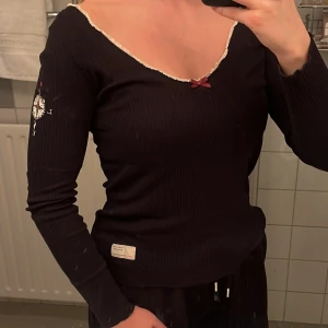 Svart långärmad topp från Odd Molly - Snygg svart långärmad topp från Odd Molly med en söt rosett vid halsringningen. Toppen har en v-ringad design med spetsdetaljer längs kanterna. 