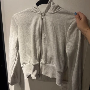 Grå hoodie från Gina Tricot - Säljer en stilren grå hoodie från Gina Tricot i storlek L. Den har en dragkedja framtill och en bekväm huva. Perfekt för en avslappnad look. Passar en M / S med.